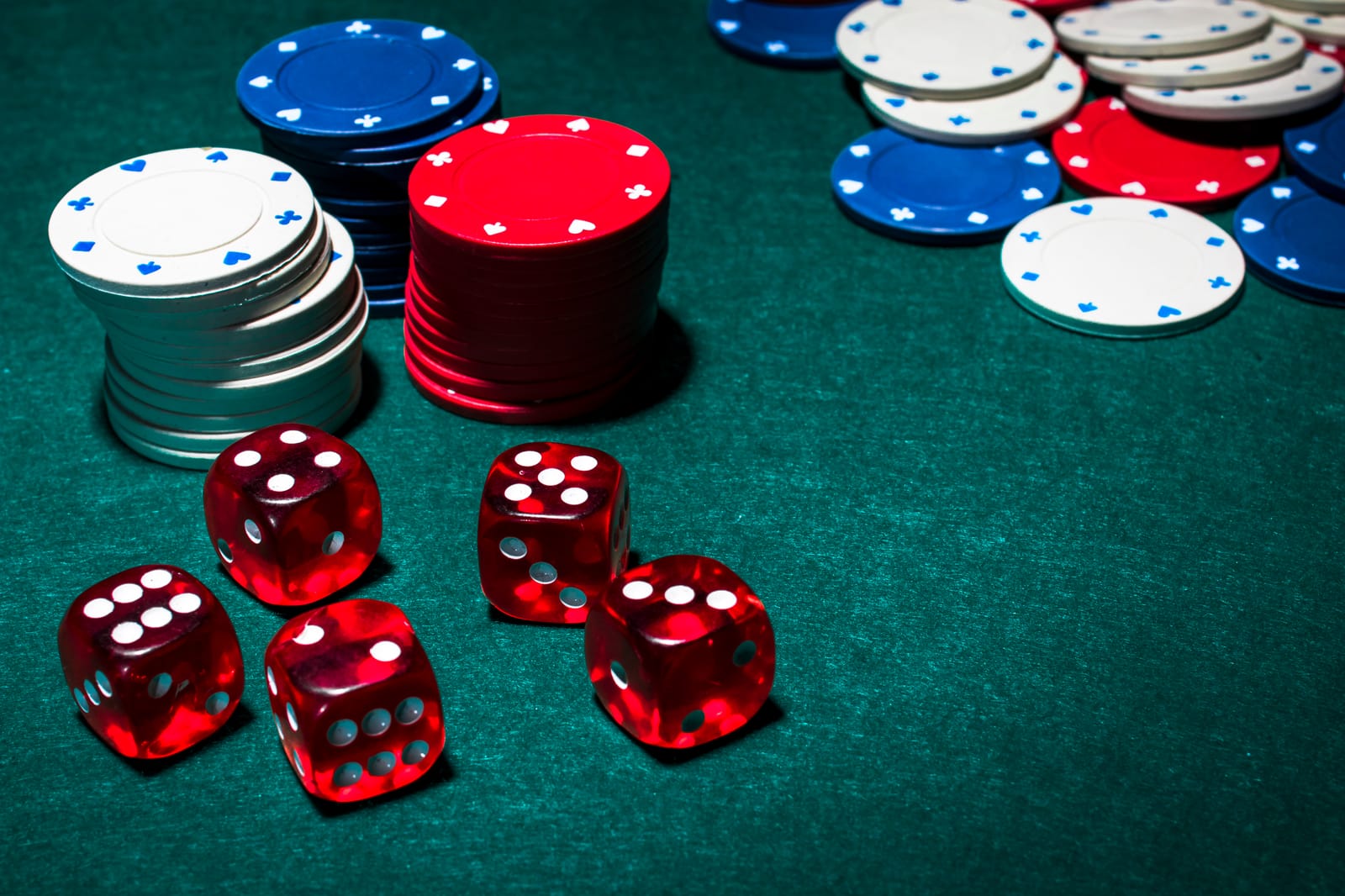 Fichas de casino y dados rojos sobre el tapete verde de una mesa de juego