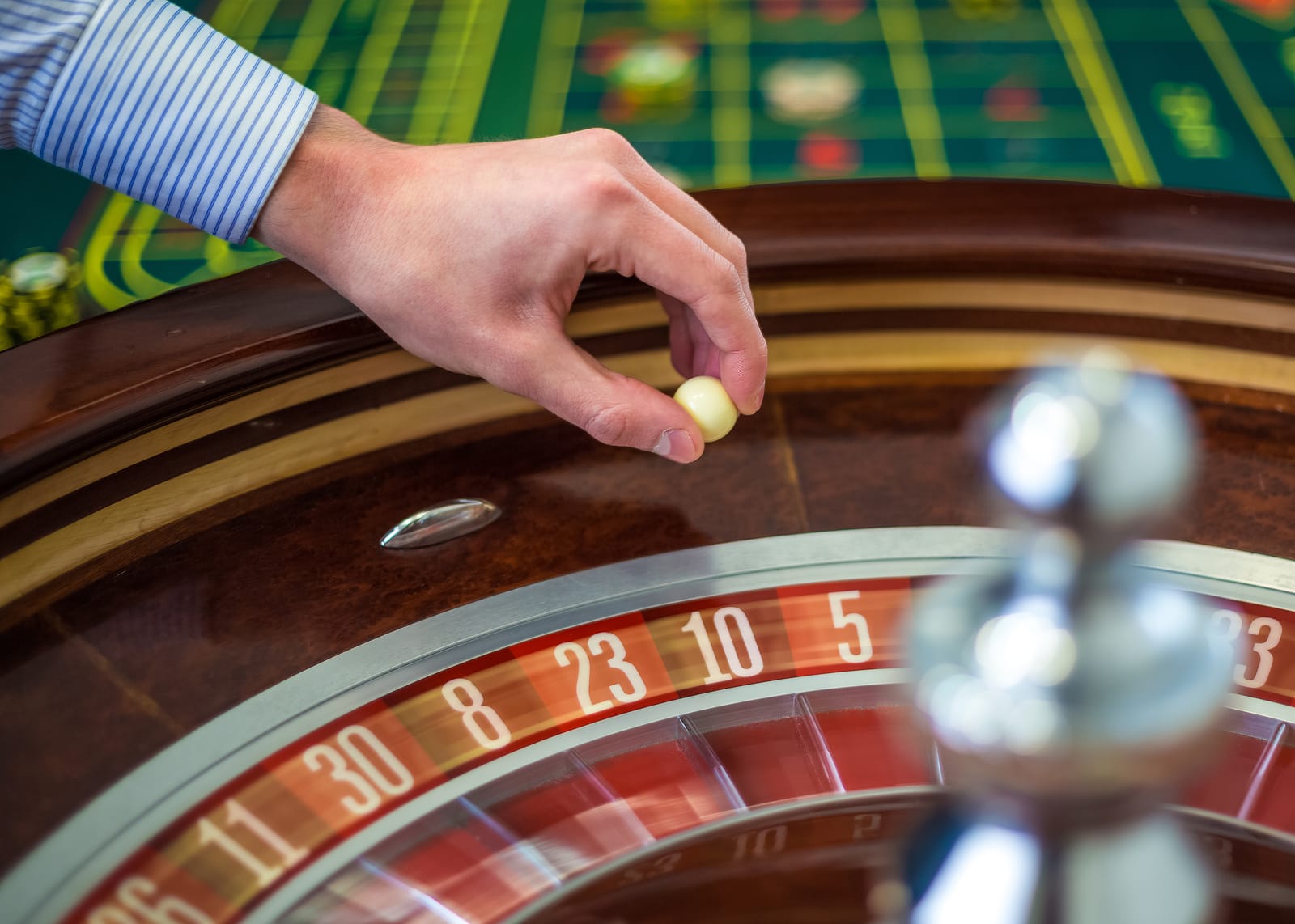 Mano del crupier con la bola junto a la rueda de una ruleta de casino