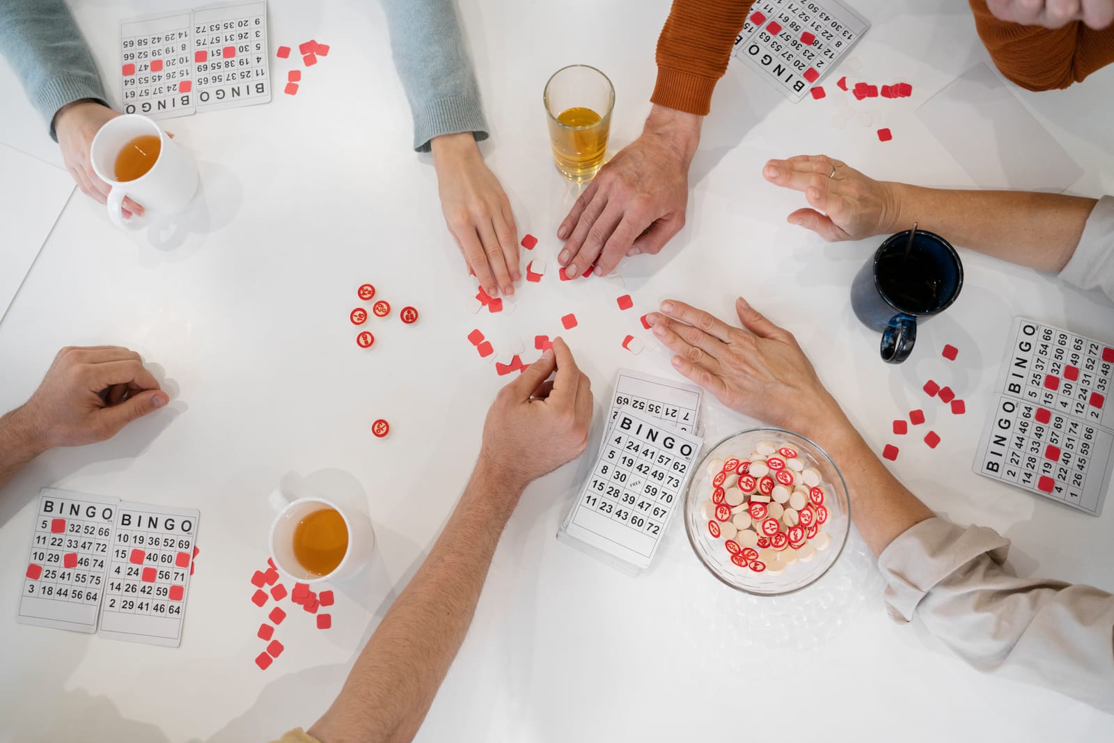 Un grupo juega al bingo alrededor de una mesa con cartones y fichas rojas